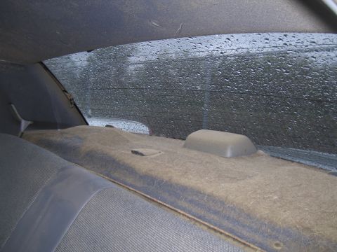 1991 Ford LTD Crown Victoria - The interior rear of a car shows a dusty parcel shelf and a rear window covered in raindrops.