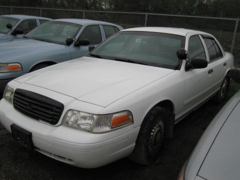 1991 Ford LTD Crown Victoria - A white police car is parked in a lot with other vehicles. The car is viewed from the front right side.