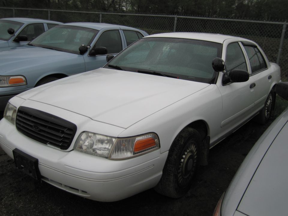 White police car, 3/4 front view. Another police car is visible to the left