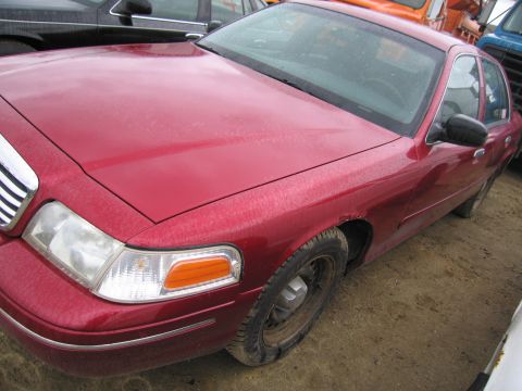 1991 Ford LTD Crown Victoria - This red sedan shows signs of rust on the front fender. The vehicle is parked outdoors with other vehicles visible.