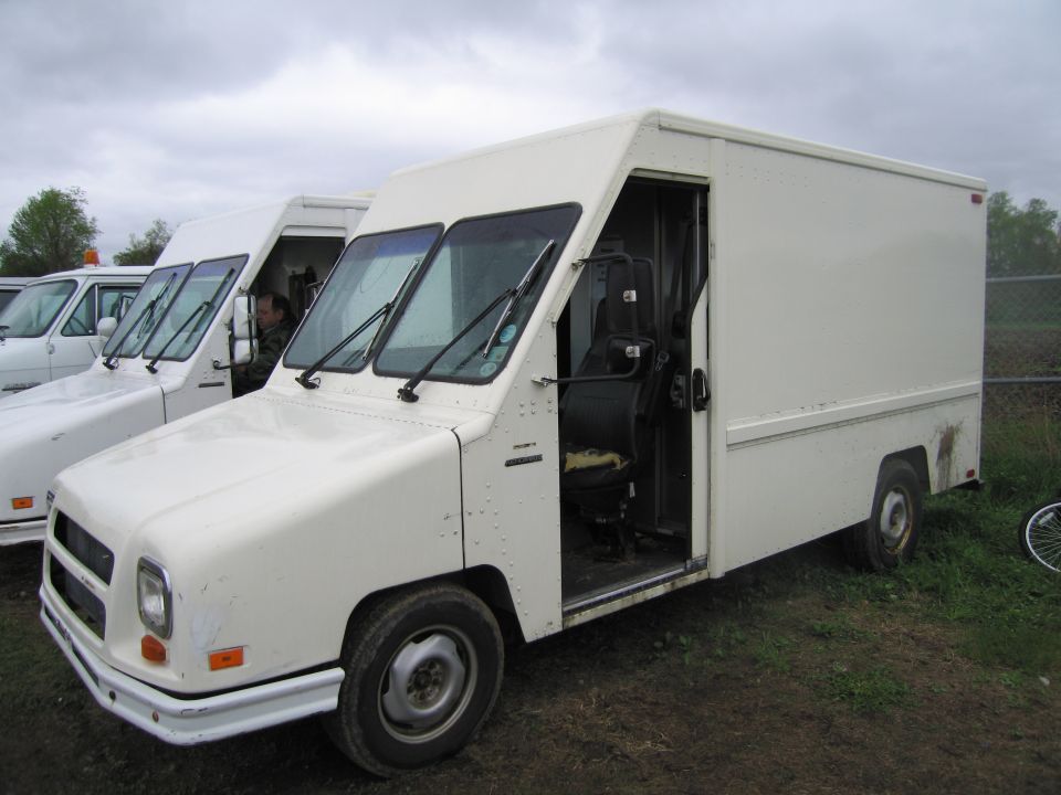 White step van parked next to other similar vans. Driver's side door is open