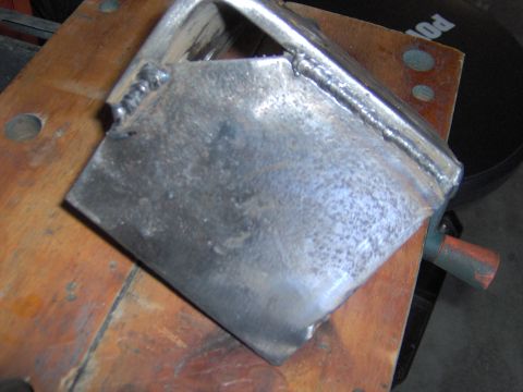 1993 Ford Bronco - A close-up view of a custom-welded metal bracket resting on a wooden workbench.