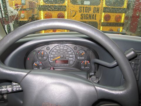 1991 Ford LTD Crown Victoria - The interior of a vehicle shows the dashboard and steering wheel, with two yellow school buses visible through the rain-streaked windshield.