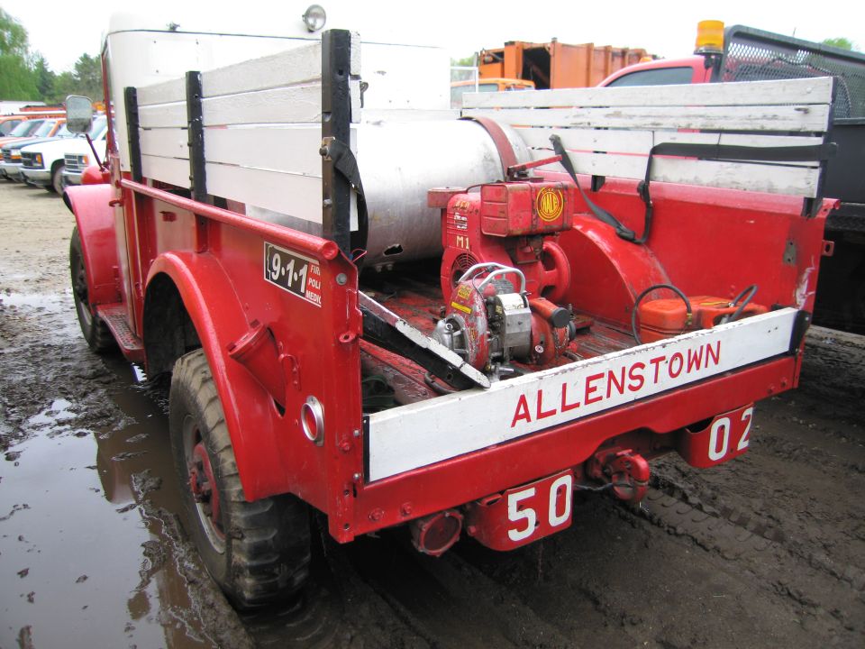 Red fire truck with white wooden bed sides, a large tank, and two engines. Text reads "ALLENSTOWN 50 02"