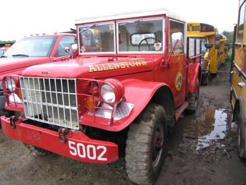 1991 Ford LTD Crown Victoria - A vintage red fire truck is parked in a muddy lot next to a line of yellow school buses.