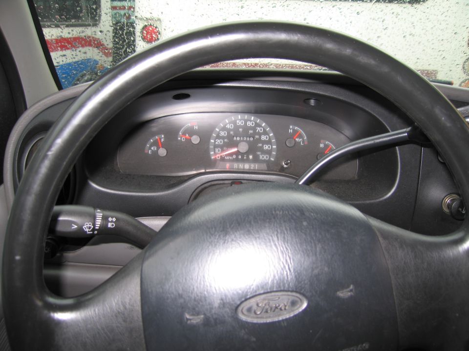 Ford steering wheel and dashboard with odometer showing 49133 miles. A truck is visible through the wet windshield