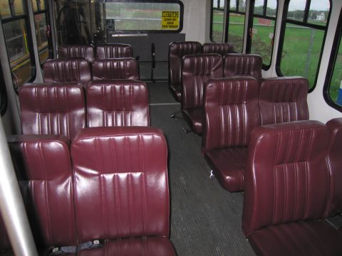 1991 Ford LTD Crown Victoria - The interior of a bus features rows of maroon vinyl seats, with windows offering a view of a grassy field outside.