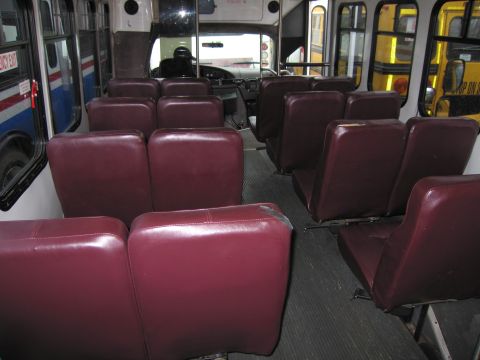 1991 Ford LTD Crown Victoria - The interior of a bus shows rows of maroon seats, with an emergency exit sign visible on the left side.