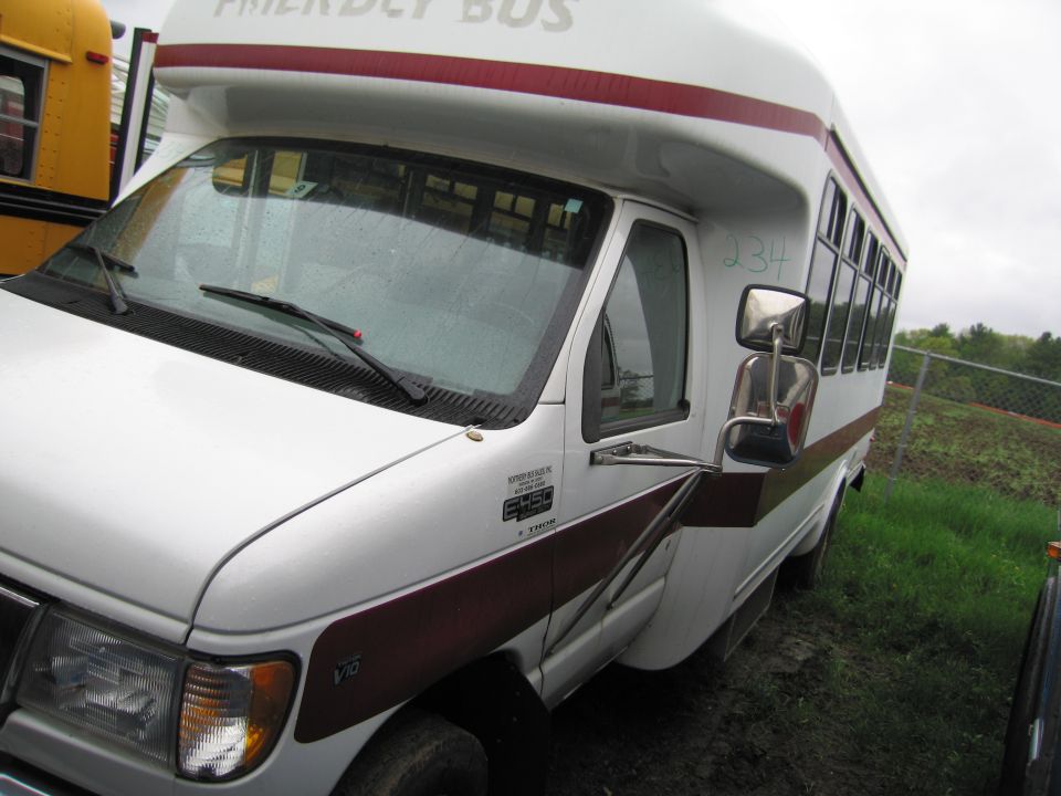 White bus with maroon stripe and "FRIENDLY BUS" text, parked next to a yellow school bus