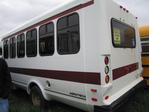 1991 Ford LTD Crown Victoria - White passenger shuttle bus parked outdoors, with another yellow bus visible to the right.