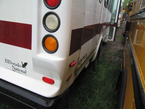 1991 Ford LTD Crown Victoria - The rear of a white ElDorado National bus is visible, its taillights and branding. Another vehicle is parked closely to its side.