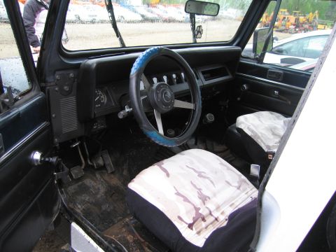 1991 Ford LTD Crown Victoria - The interior of a Jeep shows camouflage seat covers and a blue steering wheel cover, with a dirty floor.