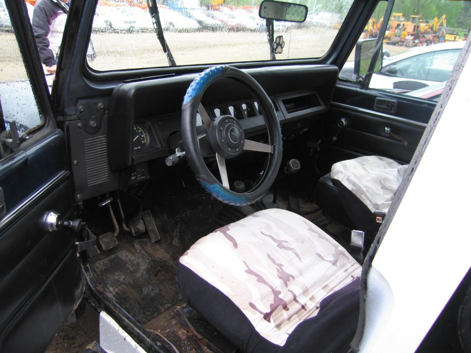 Interior of a Jeep with camouflage seat covers and a blue steering wheel cover. Floor is dirty