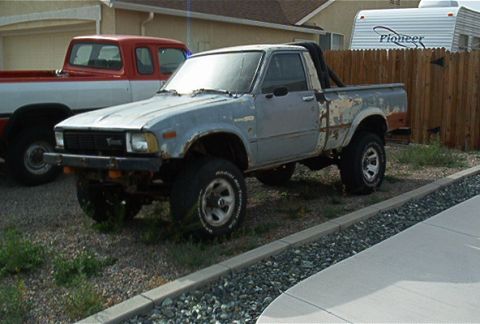 1982 Toyota 4Runner - A weathered Toyota pickup truck sits parked in a gravel lot next to another truck.