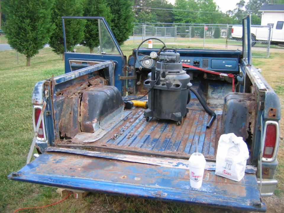 Blue 1974 Ford Bronco rear view with open tailgate, showing rusty bed and interior with shop vac