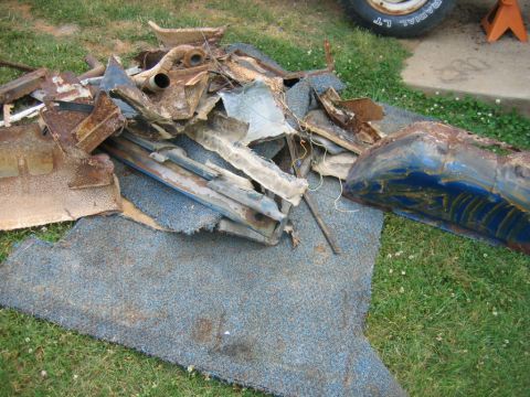 1992 Ford Mustang - A collection of heavily rusted car parts and blue carpet are scattered on the grass.