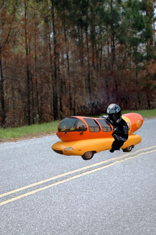 Oscar Mayer Wienermobile driving down a road with a person in motorcycle gear riding it