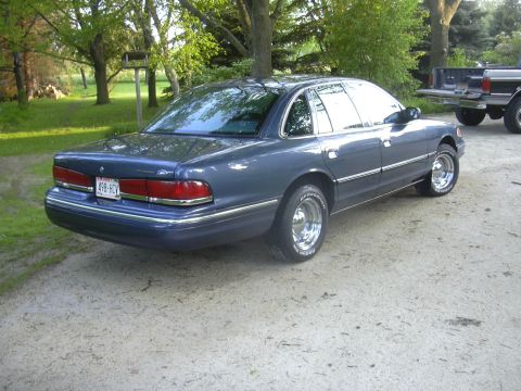 1996 Ford Crown Victoria - A blue 1996 Ford Crown Victoria sedan is parked on a dirt road with a pickup truck in the background.