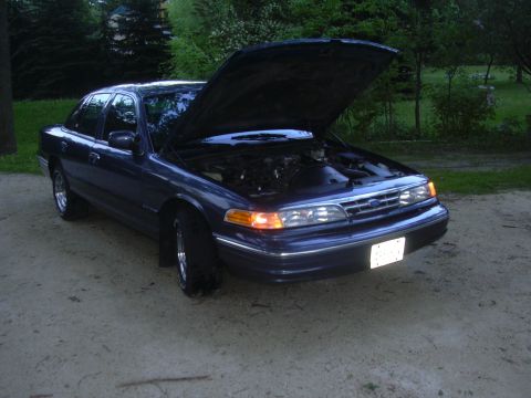 1996 Ford Crown Victoria - The front of a dark blue sedan is visible with its hood open, revealing the engine compartment.