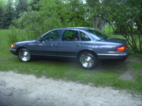 1996 Ford Crown Victoria - A blue sedan is parked on a grassy area with trees in the background.