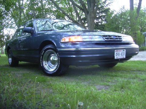 1996 Ford Crown Victoria - Dark blue sedan with chrome wheels and a Wisconsin license plate 498-HCV parked on grass.