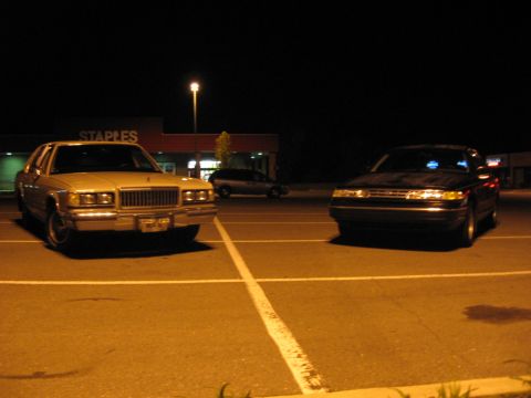 1988 Mercury Grand Marquis - Two cars are parked in a lot at night, with a Staples store in the background.