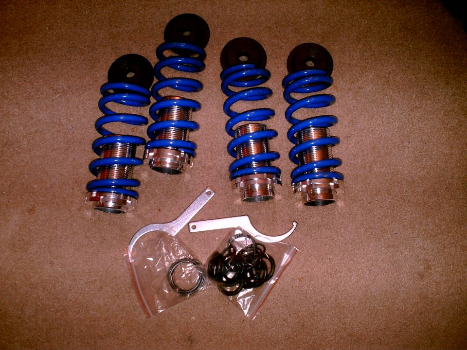 Four blue coilover suspension units with adjustment wrenches and hardware