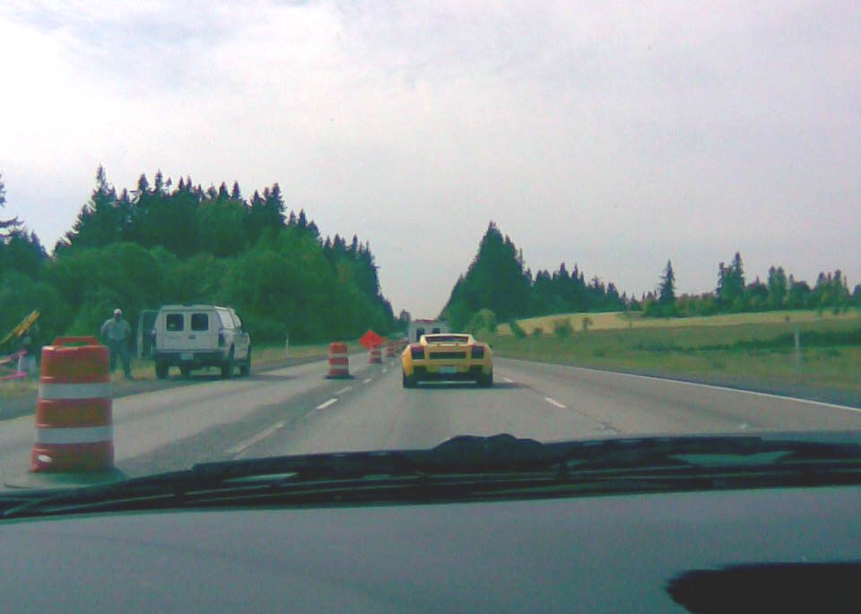 Yellow sports car seen from behind on a highway with construction barrels