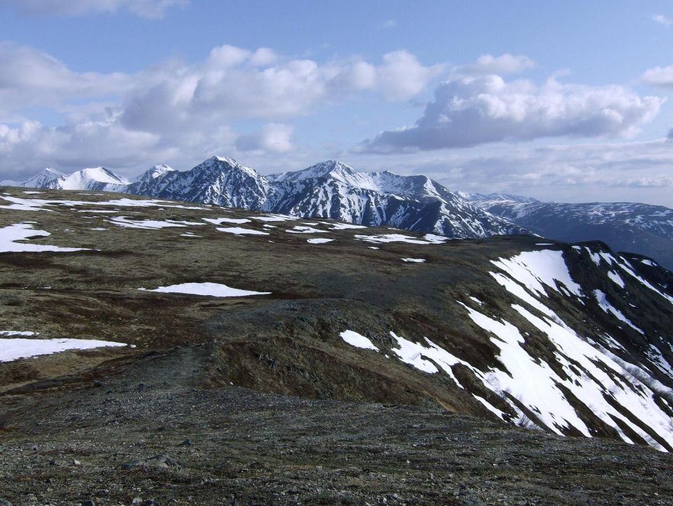 Snow-capped mountains under a cloudy sky, with rocky, snow-dusted terrain in the foreground
