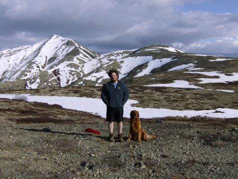 1982 Chevrolet C/K Pickup - A man and his dog pose for a photo in a vast, landscape with snow-capped mountains under a cloudy sky.