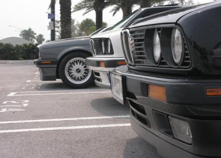 1989 BMW 3 Series - Three BMW 3 Series cars are parked in a lot, with a close-up on the front of the black car.