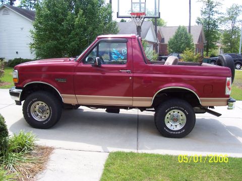 1994 Ford Bronco - Side profile of a red 1994 Ford Bronco with tan trim, showing its removable top configuration.