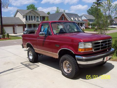 1994 Ford Bronco - This red Ford Bronco with tan trim is parked in a suburban driveway.