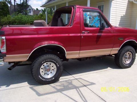 1994 Ford Bronco - Side view of a red 1994 Ford Bronco with its top removed, parked outdoors.