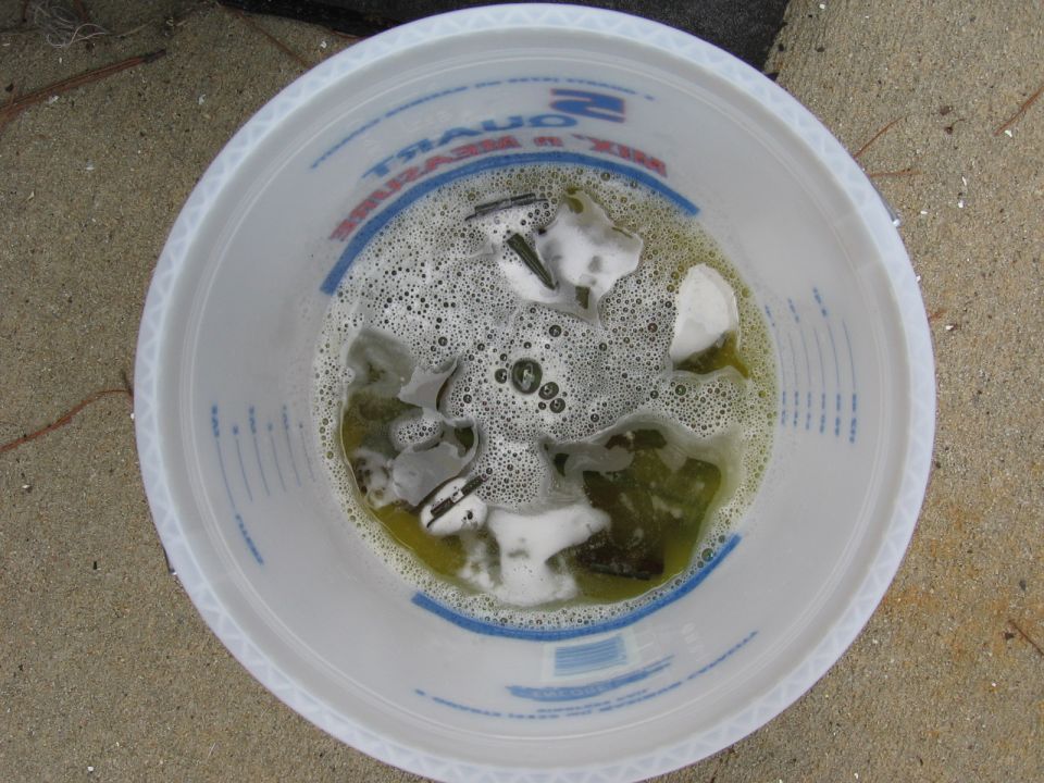 Various metal parts soaking in soapy water inside a white plastic bucket