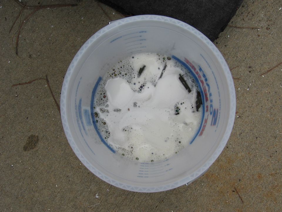 Bucket with soapy water and dark parts soaking. Some bubbles are visible