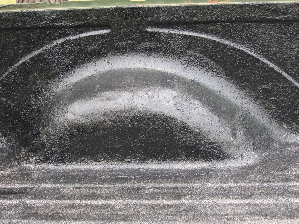 Truck bed liner showing a black textured wheel well and ribbed floor