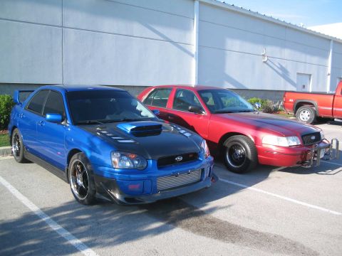2001 Ford Crown Victoria - A blue Subaru WRX and a red Ford Crown Victoria are parked side-by-side in a parking lot.