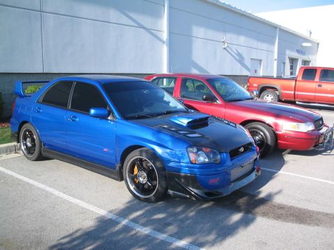 2001 Ford Crown Victoria - A blue Subaru WRX STI is parked in a lot next to a red sedan and a red pickup truck.