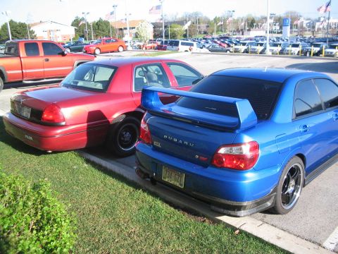 2001 Ford Crown Victoria - A red 2001 Ford Crown Victoria is parked next to a blue Subaru WRX STI.
