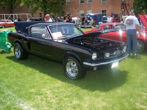 1972 Ford Ranchero - A black 1965 Ford Mustang Fastback is displayed at a car show with its hood open.
