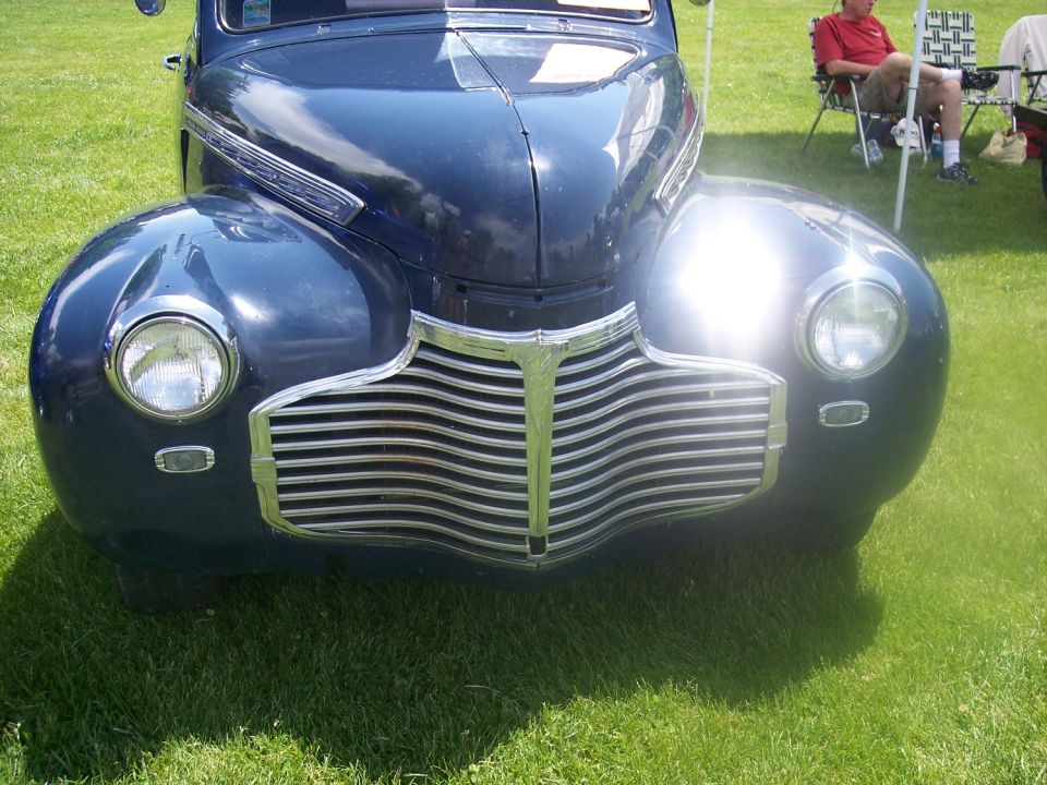 Front view of a dark blue vintage car with a chrome grille and round headlights