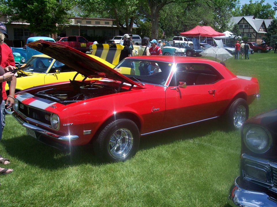 red 1967 Camaro with hood open, parked on grass at a car show