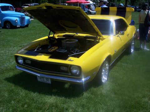 1972 Ford Ranchero - A bright yellow 1968 Chevrolet Camaro is displayed with its hood open at a car show, revealing the engine and black racing stripes on the h…