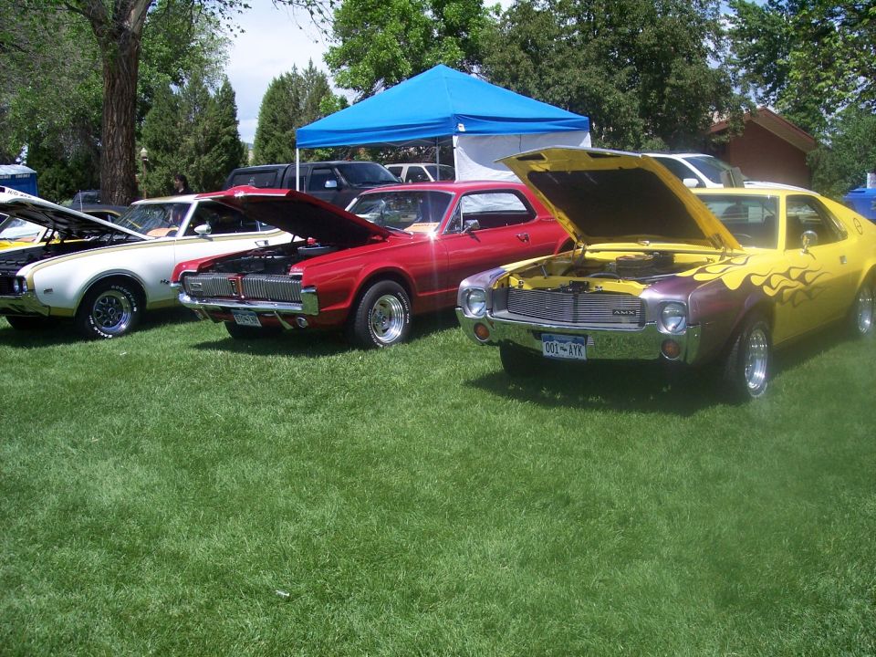 three classic cars with hoods up at a car show
