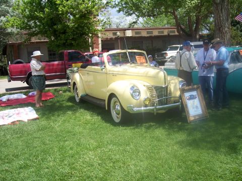 1972 Ford Ranchero - A yellow 1940 Ford convertible is displayed at a car show with several people around it.