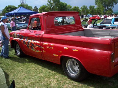 1972 Ford Ranchero - A red pickup truck with flame decals is parked on grass at a car show with other vehicles in the background.