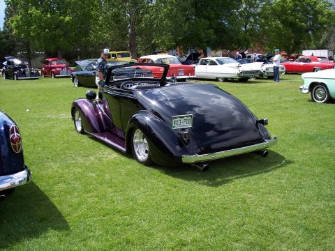 1972 Ford Ranchero - A black convertible hot rod with purple accents is displayed at a car show with other vehicles in the background.