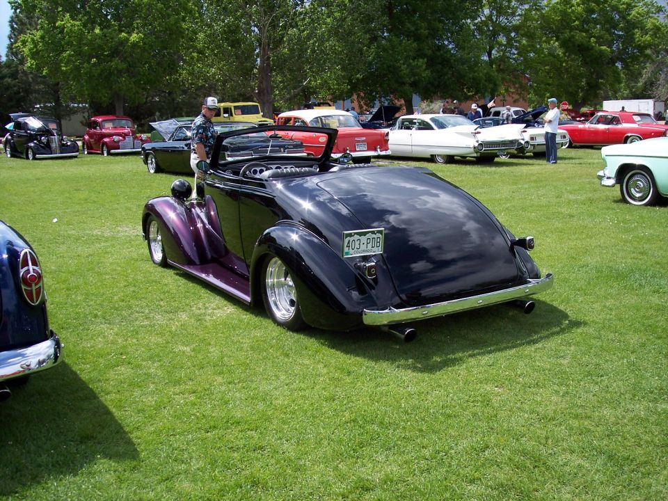 Black convertible hot rod with purple accents and a license plate reading 403-P08 parked on grass