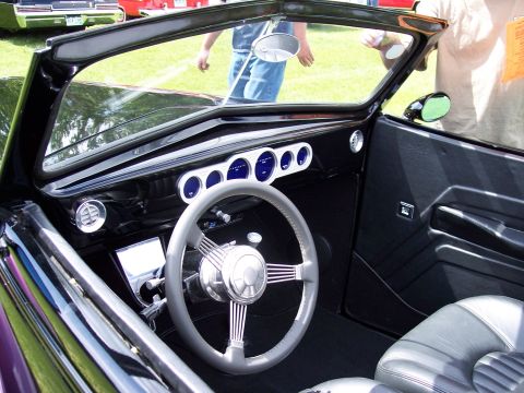 1972 Ford Ranchero - The interior of a black convertible features custom gauges and a unique steering wheel, seen at a car show.